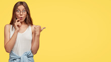 Surprised Beautiful Young Woman Stares With Bugged Eyes, Keeps Jaw From Amazement, Asks Question About What She Sees, Feels Impressed, Wears Casual White Vest, Isolated Over Yellow Background
