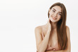 © Cookie Studio - Tender and caring feminine innocent girl with long brown healthy hair tilting head flirty smiling gently and touching neck feeling shy and sensual posing in beige dress over gray background