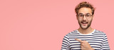 Fototapeta  - Cheerful curly man with bristle, points left, wears casual clothes and spectacles, has satisfied expression, shows free space for your slogan, promotional content or advertisemet. Look aside there