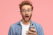 © wayhome.studio  - Stupefied Caucasian guy with surprised expression, holds cellular in hands, recieves unexpected notification, wears round spectacles, keeps mouth opened, isolated over pink studio background