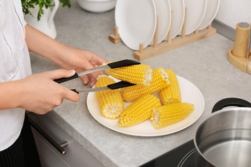 Sticker - Woman taking corn cob from plate with tongs in kitchen, closeup