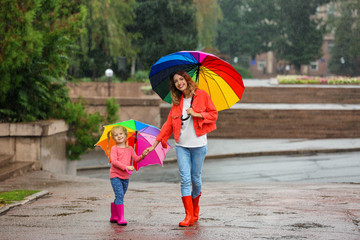 Wall Mural - Happy mother and daughter with bright umbrella under rain outdoors