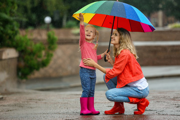 Happy mother and daughter with bright umbrella under rain outdoors