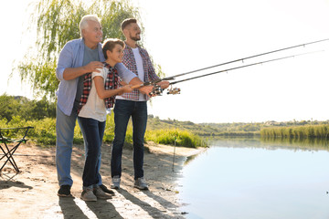 Happy family fishing together from riverside on sunny day