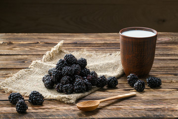 Wall Mural - Heap of fresh dewberry on sackcloth table-napkin and clay cup with milk on wooden table