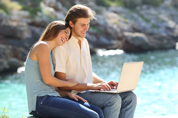 Wall Mural - Happy couple are using a laptop on vacation on the beach