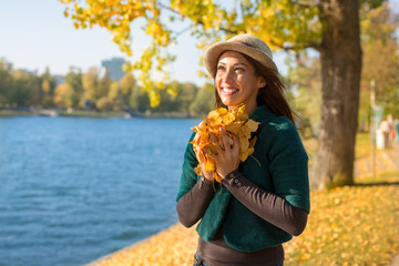 Wall Mural - Beautiful young woman holding autumn leaves in her hand while smiling