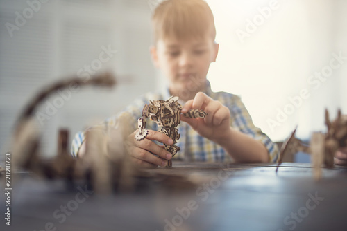 Fotografie, Tablou Concentrated kid sitting at the table and looking concentrated while creating un