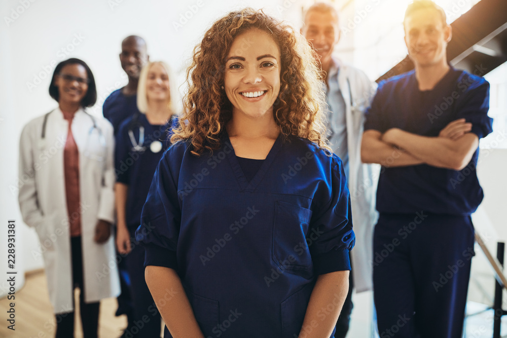 Smiling female doctor standing with medical colleagues in a hosp - obrazy, fototapety, plakaty 