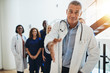 © Flamingo Images - Mature doctor extending a handshake with hospital staff behind h