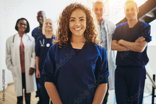 Cuadros en Lienzo Smiling female doctor standing with medical colleagues in a hosp