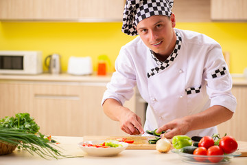 Young professional cook preparing salad at kitchen