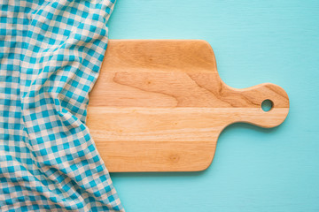 Top view of unused brand new brown handmade wooden cutting board and blue napkins on blue wooden table background - Food and kitchen concept