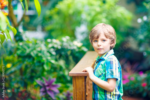 Foto Little blond preschool kid boy discovering flowers, plants and butterflies at botanic garden