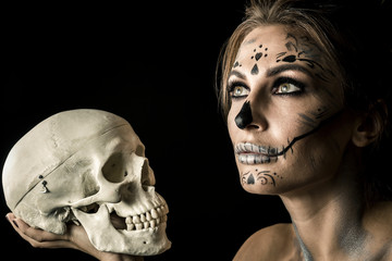 Wall Mural - Portrait of the woman with halloween makeup close up. Playiong with skull. Isolated image on black background with beautiful studio light.