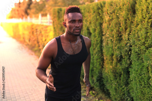 Fotografía African man in sports clothing running while exercising outdoors, at sunset or sunrise