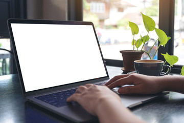 Mockup image of a woman's hands using and typing on laptop with blank white desktop screen with coffee cup on wooden table in cafe