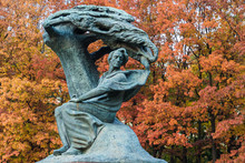 Monument To Fryderyk Chopin, Famous Polish Composer, In Royal Baths Park, The Best-known Polish Sculpture In The World By Waclaw Szymanowski On The Red Trees Background.