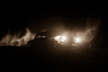 Silhouette of old vintage car in dark foggy toned background with glowing lights in low light.