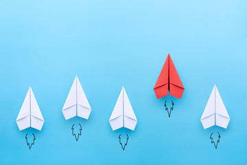 red paper plane leading among a white planes on blue background. business competition and leadership