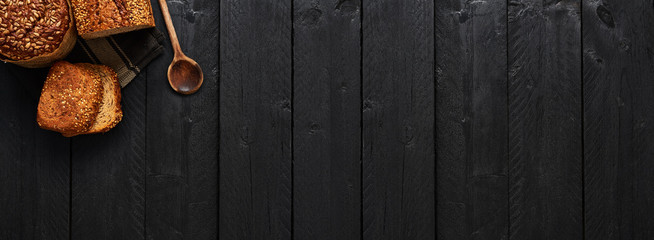 Various crusty whole wheat bread and slices of bread on black wooden table. Top view with copy space for text, menu or recipes. Banner.