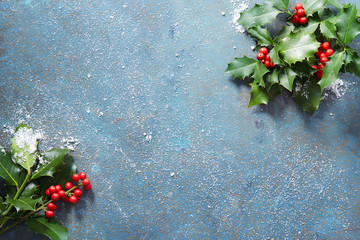 Christmas background, holly leaves and red berries, covered in snow with copy space.