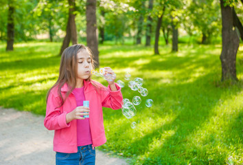 A little girl blowing soap bubbles in summer park