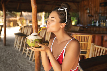 Poster - Young and sexy woman sitting in authentic beach bar with a coconut drink