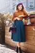 © Victoria Fox - Outdoor full body fashion portrait of young beautiful happy smiling woman wearing stylish  beret, orange turtleneck, midi green blue skirt, ankle boots, holding quilted purple bag, posing in street
