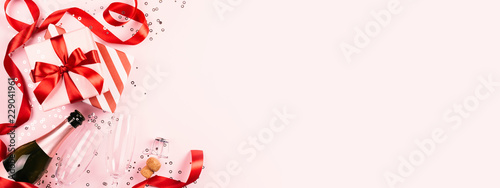 Christmas gift with red ribbon, champagne, two glasses on pink background wit...