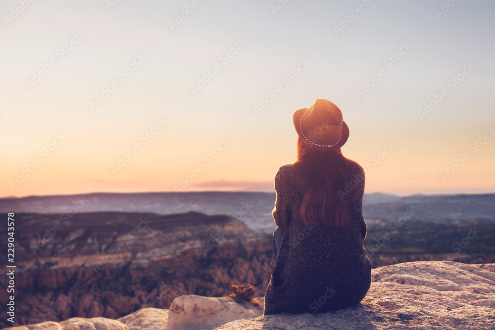 A girl in a hat on top of a hill in silence and loneliness admires a tranquil natural landscape in search of a soul. - obrazy, fototapety, plakaty 