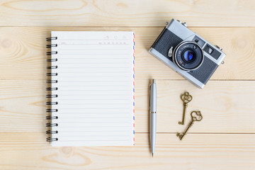 Top view from above / flat lay of blank page spiral or flipped notepad / opened diary book, old retro 35mm film camera, two vintage keys and a blue pen on a wood table, for writing plan, schedule etc.