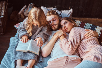 Mom, dad and daughter reading storybook together while lying on bed.