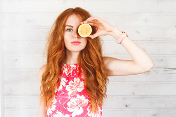 Delighted red-hair woman keep two lemons on her eyes. The portrait with a copyspace