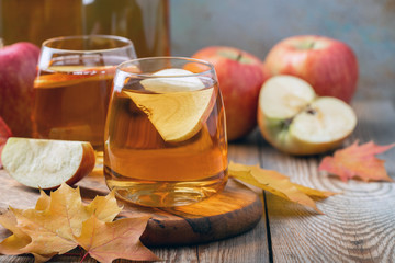 Wall Mural - Organic Apple cider or juice on a wooden table. Two glasses with drink and autumn leaves on rustic background