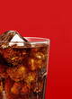Cola with ice in glass cup isolated on red background