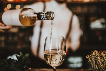 Wall Mural - Close up shot of a bartender pouring white wine into a glass. Hospitality, beverage and wine concept.