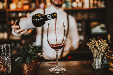 Close up shot of a bartender pouring red wine into a glass. Hospitality, beverage and wine concept.