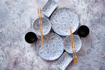 Empty oriental style ceramic bowls, plates and chopsticks on gray stone background with copy space. Top view.