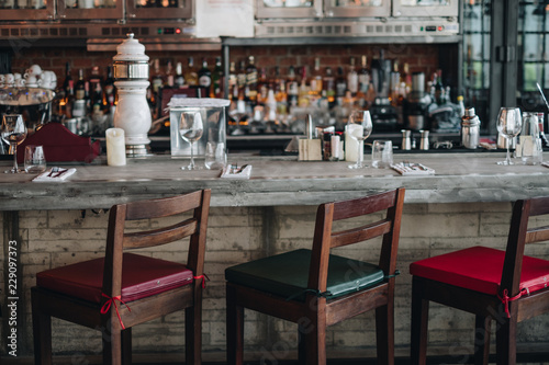 Zdjęcie XXL Drewniany barowy kontuar z defocus tłem i butelką restauracja, bar, bufet. Przygotuj zestaw szklanek, widelca i noża na stole