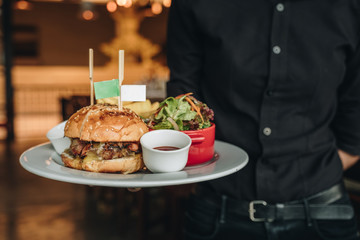 Big tasty burger with fresh salad served by waiter with black costume