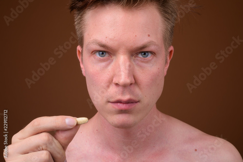 Fotografia Portrait of shirtless young man holding multi vitamin pill