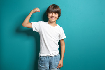 little boy in t-shirt showing muscles on color background