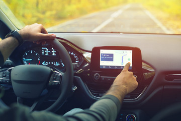 Male driver using dashboard screen maps while driving on road in autumn warm colors