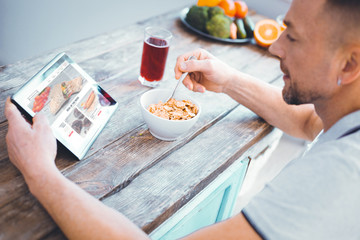 Internet connection. Nice pleasant man browsing the Internet while eating his breakfast in the kitchen