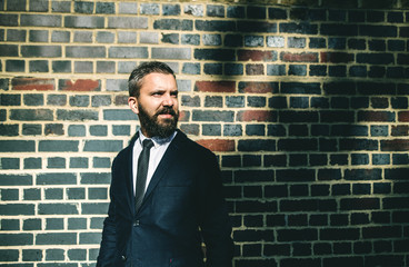 Wall Mural - Hipster businessman standing against brick wall on the street in London.