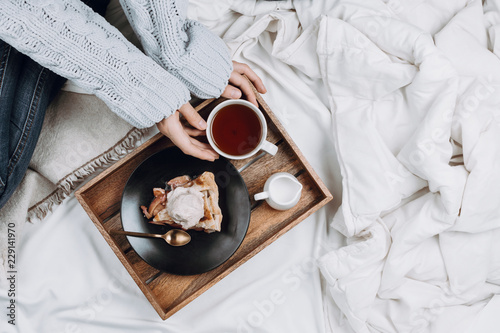 Fotografía Cozy flatlay of bed with wooden tray with pie, ice cream and black tea and woman