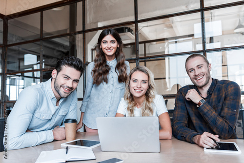 Cuadros en Lienzo happy young business colleagues working with gadgets and smiling at camera in of