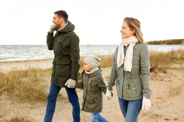 Wall Mural - family, leisure and people concept - happy mother, father and little daughter walking along autumn beach