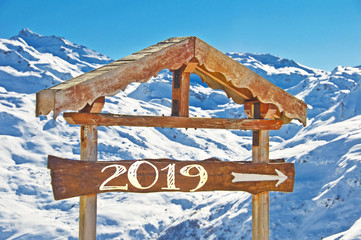 Wall Mural - 2019 written on a wooden direction sign, snow mountain landscape on the background
